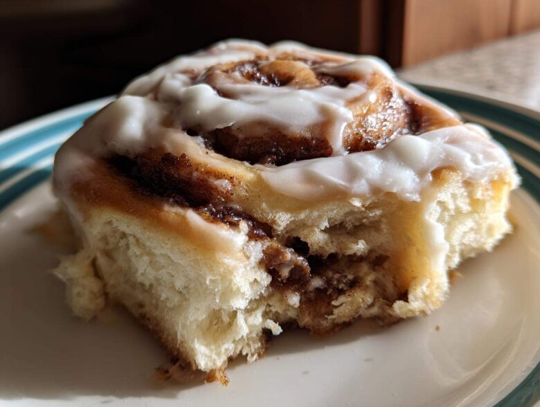 Close-up of a soft, fluffy Gluten-Free Cinnamon Rolls piece with rich cinnamon swirl and white icing.