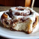 Close-up of a soft, fluffy Gluten-Free Cinnamon Rolls piece with rich cinnamon swirl and thick white icing.