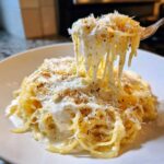 A fork lifts strands of cheesy Spaghetti Squash Alfredo, showing the creamy sauce and grated Parmesan cheese.
