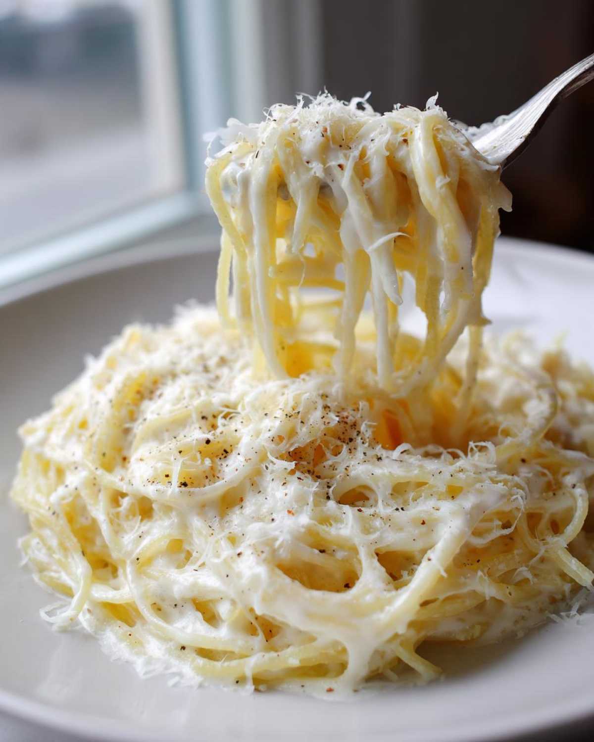 A fork lifts strands of creamy Spaghetti Squash Alfredo topped with grated Parmesan cheese and black pepper.