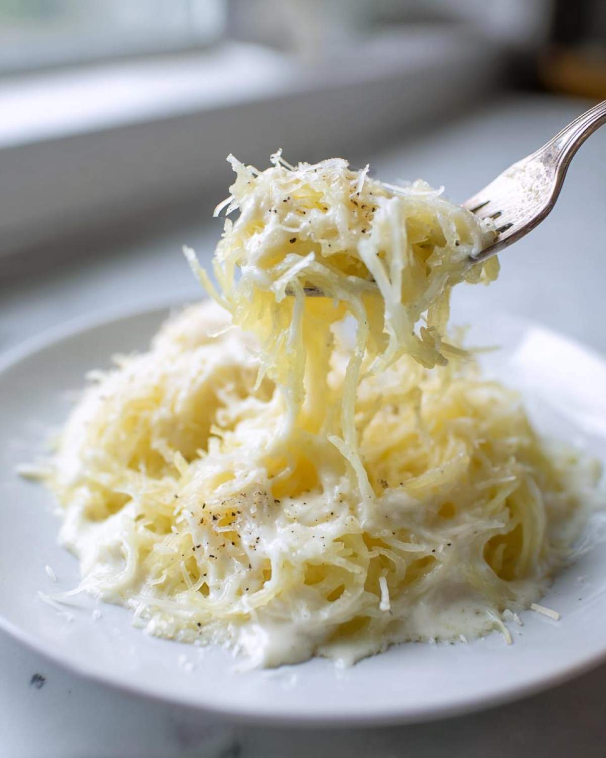 A fork lifts strands of creamy Spaghetti Squash Alfredo topped with grated Parmesan cheese and black pepper.