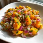 Close-up of vibrant Spicy Mango Salsa featuring diced orange mango, red onion, and green herbs in a white bowl.