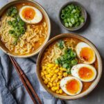 Two bowls of Spicy Miso Ramen with soft-boiled eggs, corn, and green onions on a grey surface.