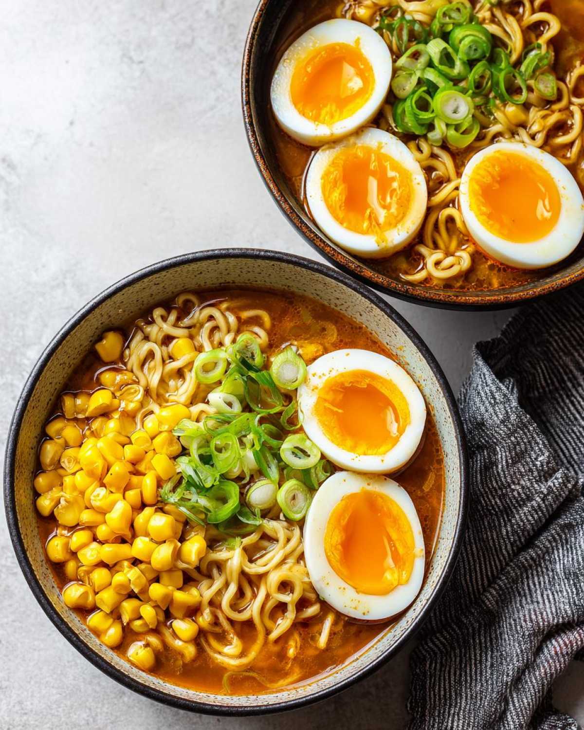 Overhead view of two bowls of Spicy Miso Ramen with soft-boiled eggs, corn, and scallions.