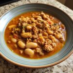 A close-up of a bowl filled with rich, orange-red Spicy Turkey White Bean Chili, featuring ground turkey and large white beans.