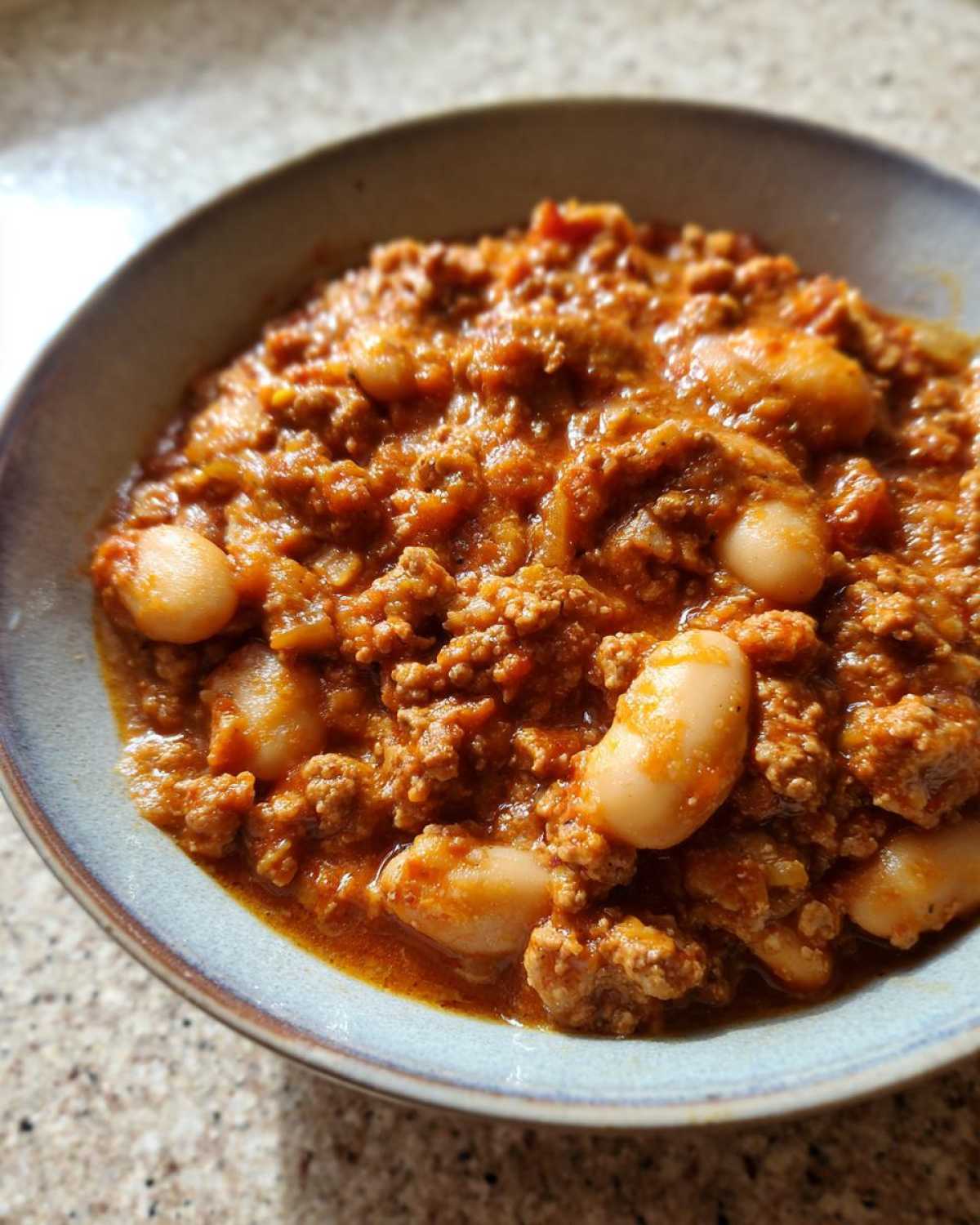 Close-up of a hearty bowl of Spicy Turkey White Bean Chili, featuring ground turkey and large white beans in a rich, reddish sauce.