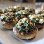 A close-up of baked Spinach and Feta Stuffed Mushrooms arranged on a white platter, featuring browned tops.