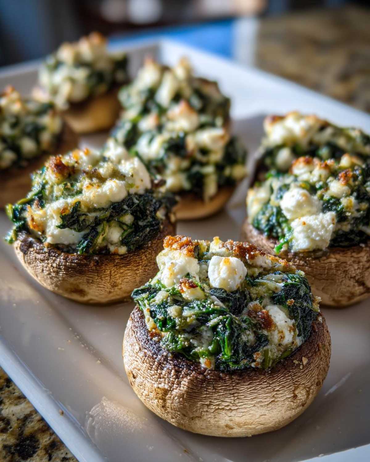 Close-up of baked Spinach and Feta Stuffed Mushrooms with browned tops served on a white platter.