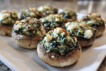 A close-up of baked Spinach and Feta Stuffed Mushrooms arranged on a white platter, featuring browned tops.