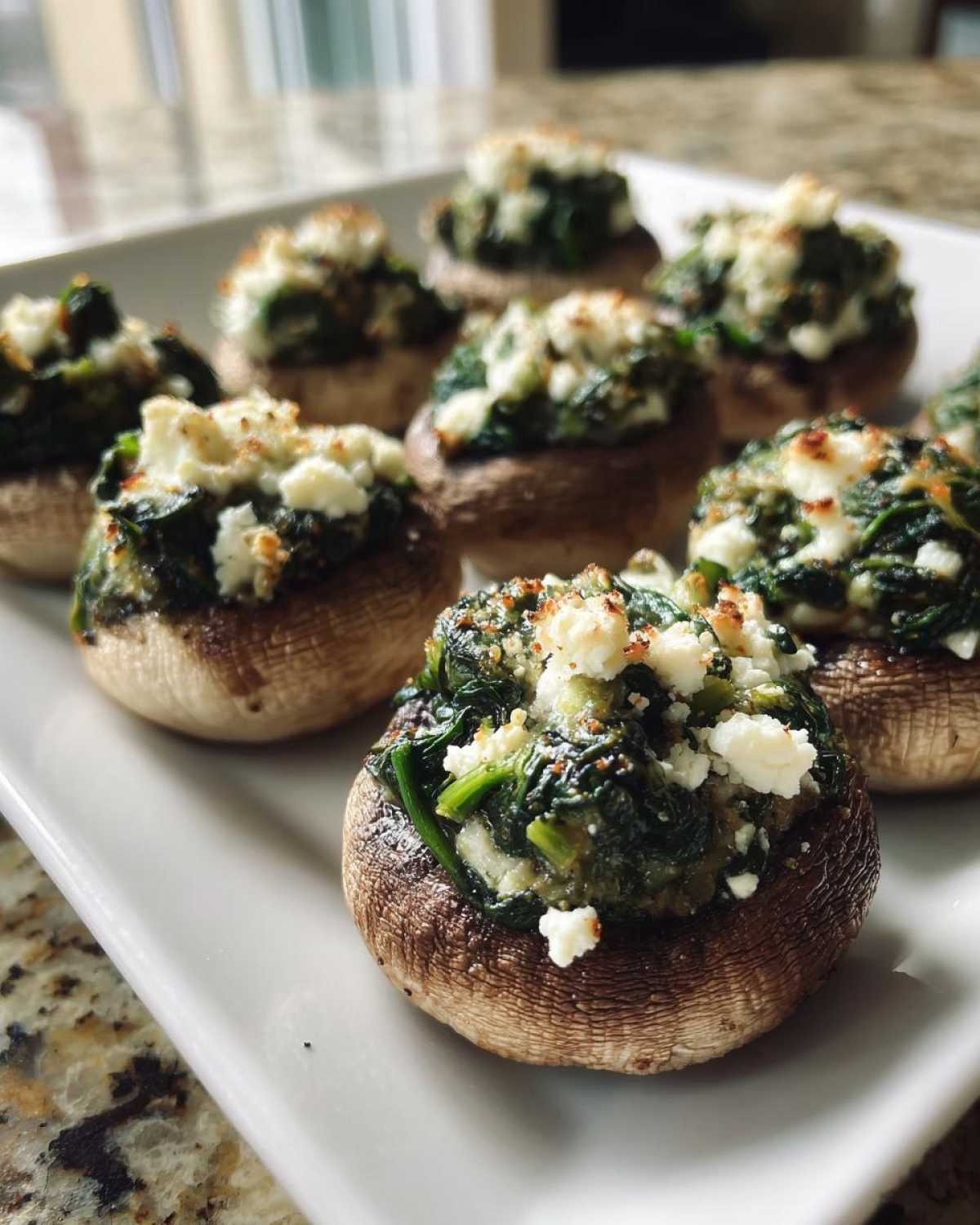 A white platter filled with freshly baked Spinach and Feta Stuffed Mushrooms, ready to serve.