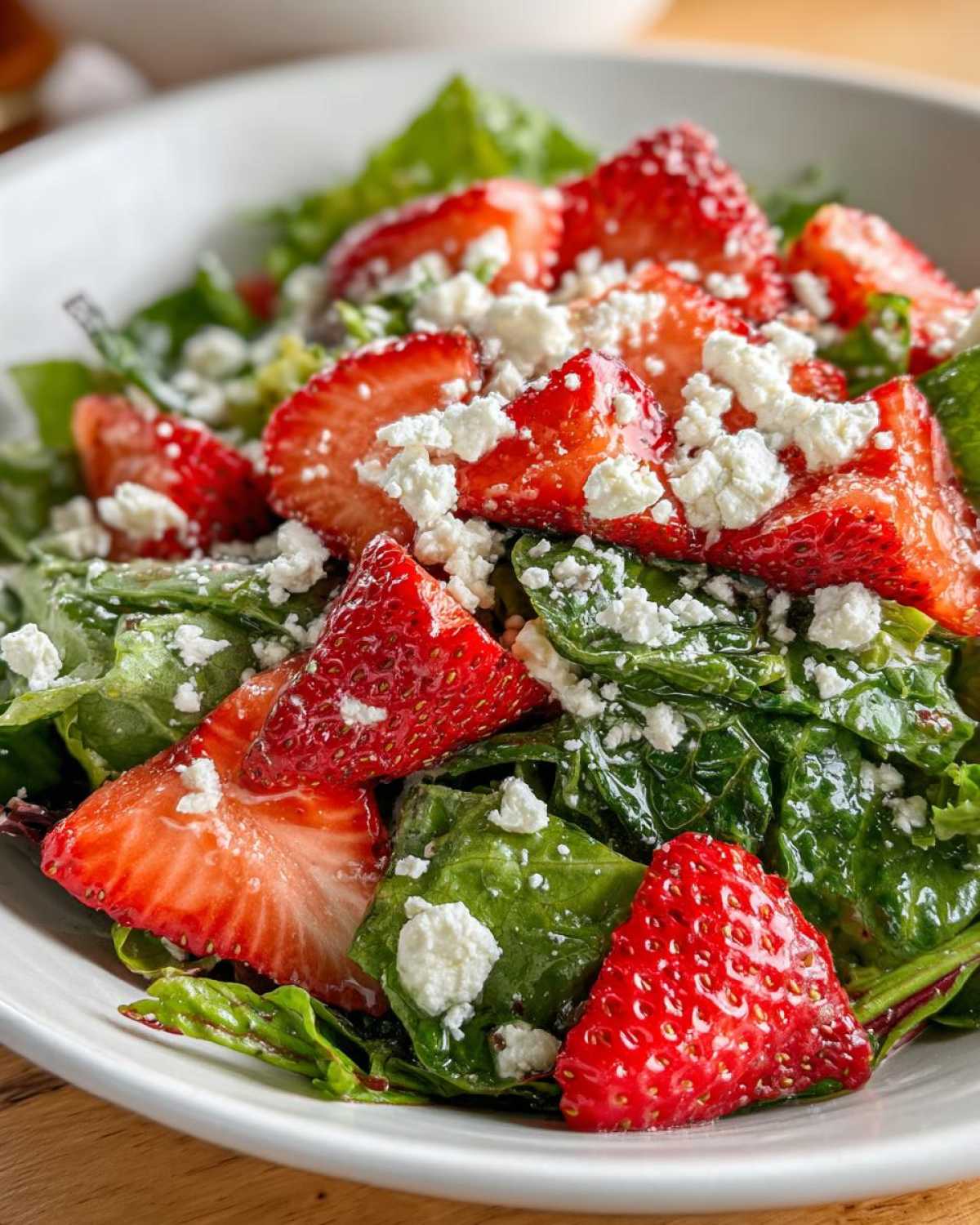 Close-up of a vibrant Spring Mix Salad with Strawberries and Goat Cheese, featuring glossy greens and bright red fruit.