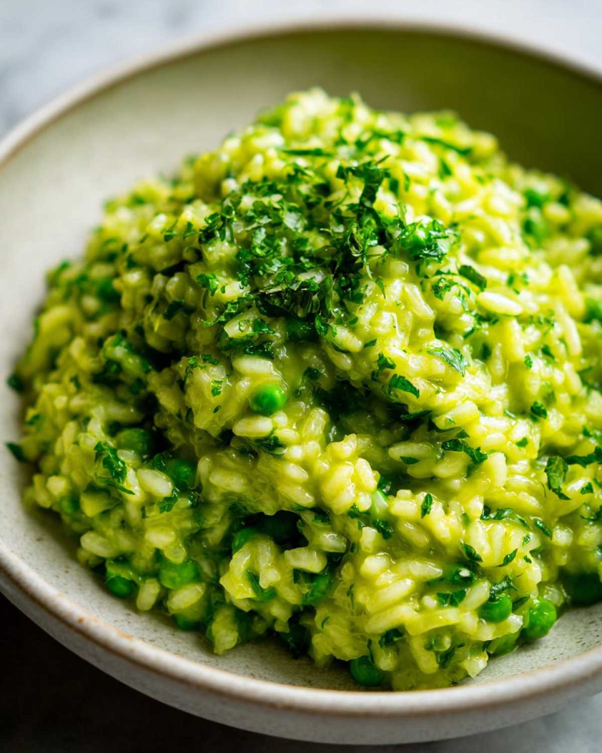 Close-up of creamy Spring Pea and Mint Risotto topped with fresh chopped herbs in a light bowl.
