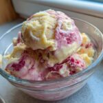 Close-up of two scoops of swirled Strawberry Banana Ice Cream in a clear glass bowl.