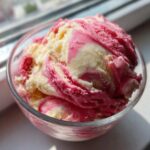 Close-up of a glass bowl filled with swirled Strawberry Banana Ice Cream, showing creamy white and bright pink ribbons.