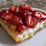 A close-up view of a flaky pastry square topped with cream cheese filling and glazed strawberries, a perfect Strawberry Cream Cheese Danish.