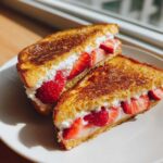 Two halves of golden-brown Strawberry Cream Cheese Stuffed French Toast filled with fresh strawberries and cream.