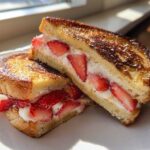 Two halves of golden-brown Strawberry Cream Cheese Stuffed French Toast piled on a white plate.