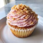 A single, perfectly frosted Strawberry Crunch Cupcakes topped with pink swirl frosting and crunchy golden crumbs.