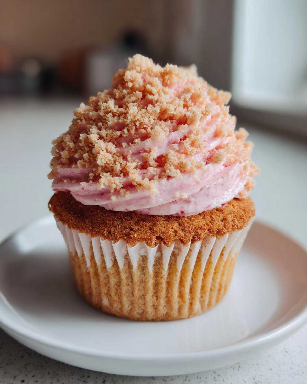 A single Strawberry Crunch Cupcakes featuring pink strawberry frosting topped with crunchy crumbs, served on a small white plate.