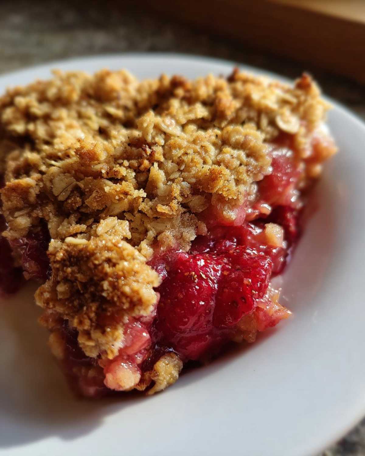 A close-up shot of a warm slice of Strawberry Rhubarb Crisp showing the bubbly fruit filling and crunchy oat topping.