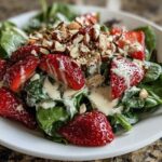 A vibrant close-up of Strawberry Spinach Salad with Poppy Seed Dressing, topped with sliced almonds.