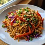 A close-up of creamy Thai Peanut Noodles with Crunchy Veggies, topped with peanuts and green onions.