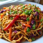 A close-up serving of Thai Peanut Noodles with Crunchy Veggies coated in peanut sauce, topped with peanuts and scallions.
