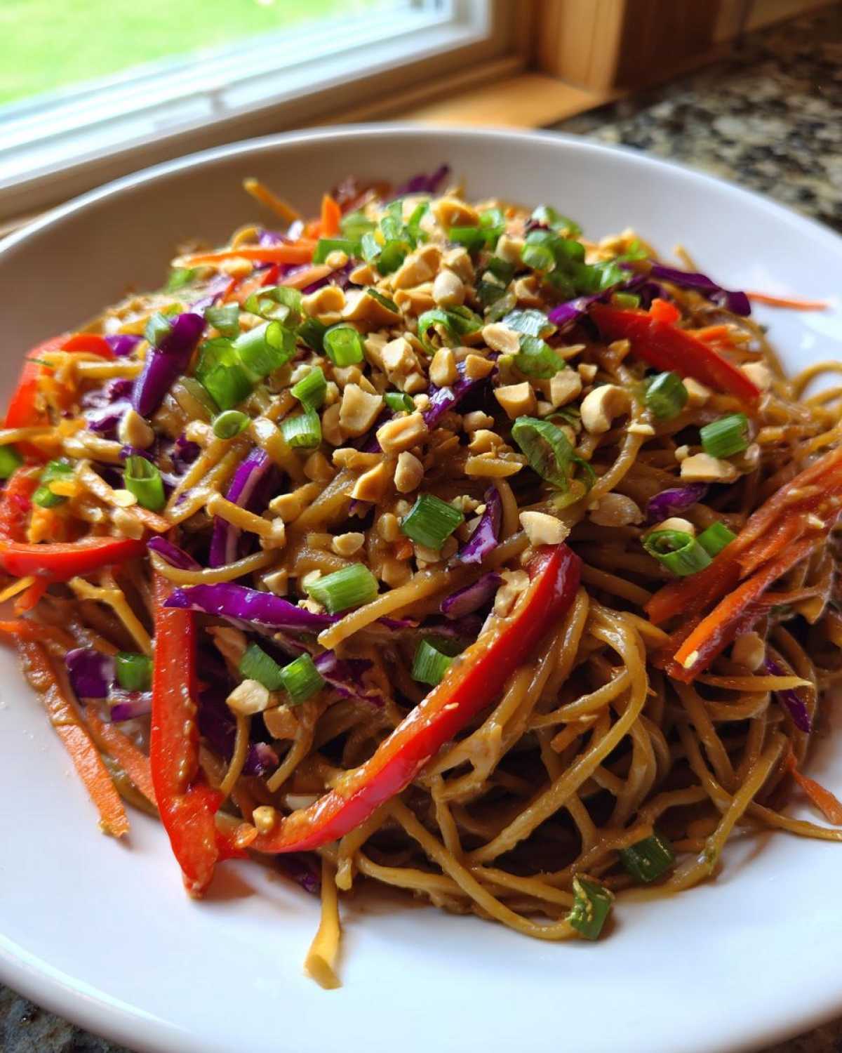 A vibrant bowl of Thai Peanut Noodles with Crunchy Veggies, topped with peanuts and green onions.