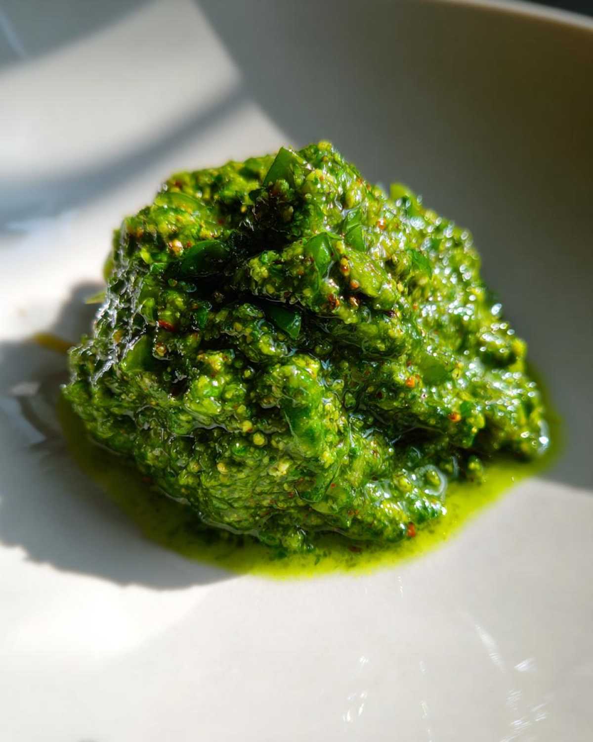 A rich, bright green mound of homemade Vegan Basil Pesto resting on a white plate, glistening with olive oil.