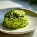 A close-up, vibrant green mound of homemade Vegan Basil Pesto resting in a shallow white bowl.