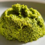 Close-up of a vibrant green mound of freshly made Vegan Basil Pesto on a white plate.