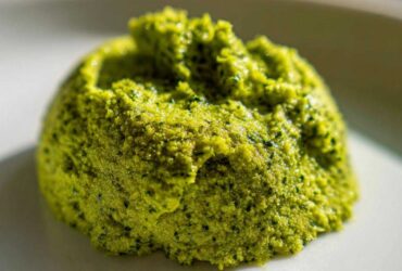 Close-up of a vibrant green mound of freshly made Vegan Basil Pesto on a white plate.