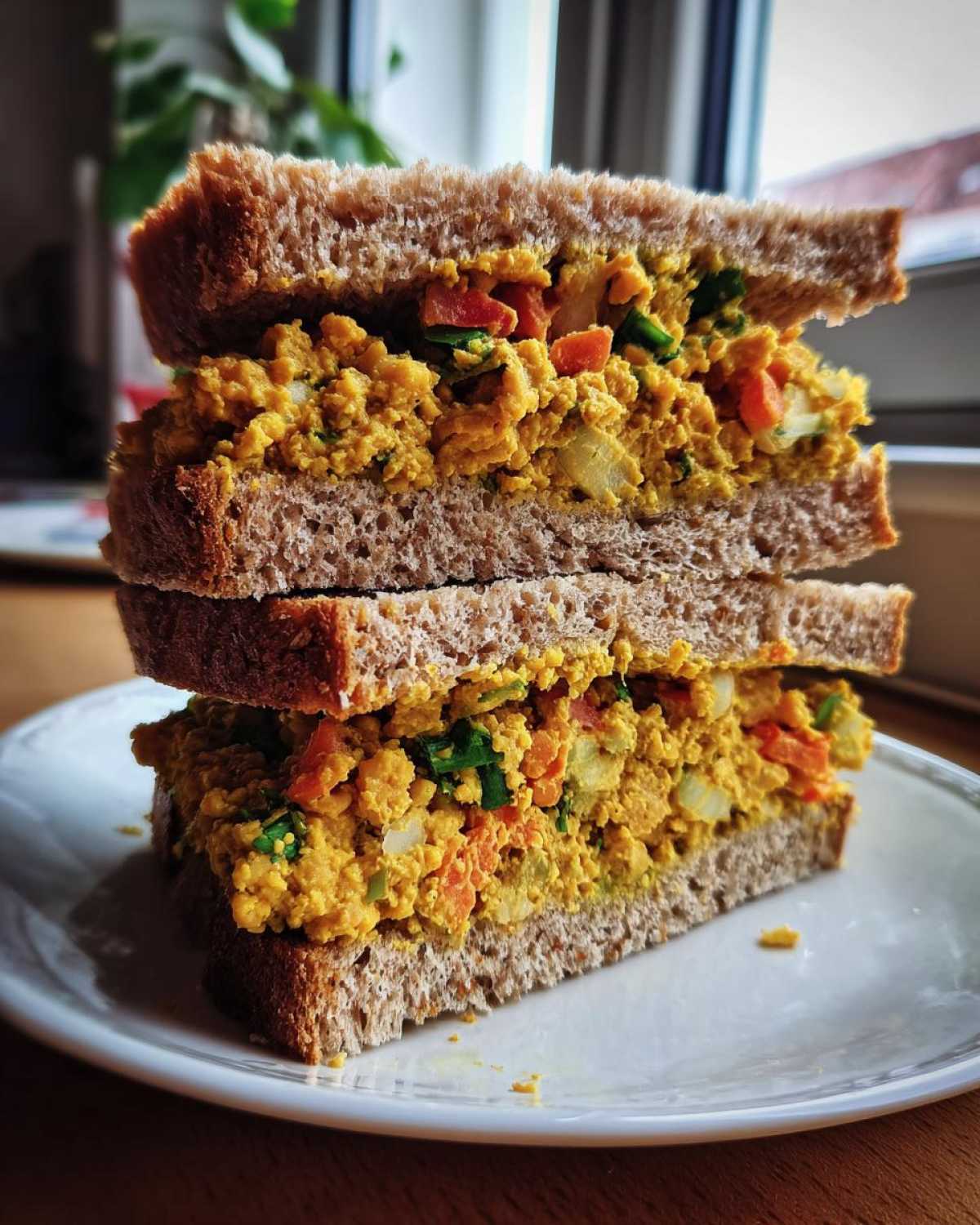 Close-up of a stacked Vegan Chickpea Salad Sandwich on whole wheat bread, showing the bright yellow filling with visible chopped vegetables.
