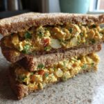 A stacked, halved Vegan Chickpea Salad Sandwich made with whole wheat bread, showing the creamy, yellow chickpea filling.