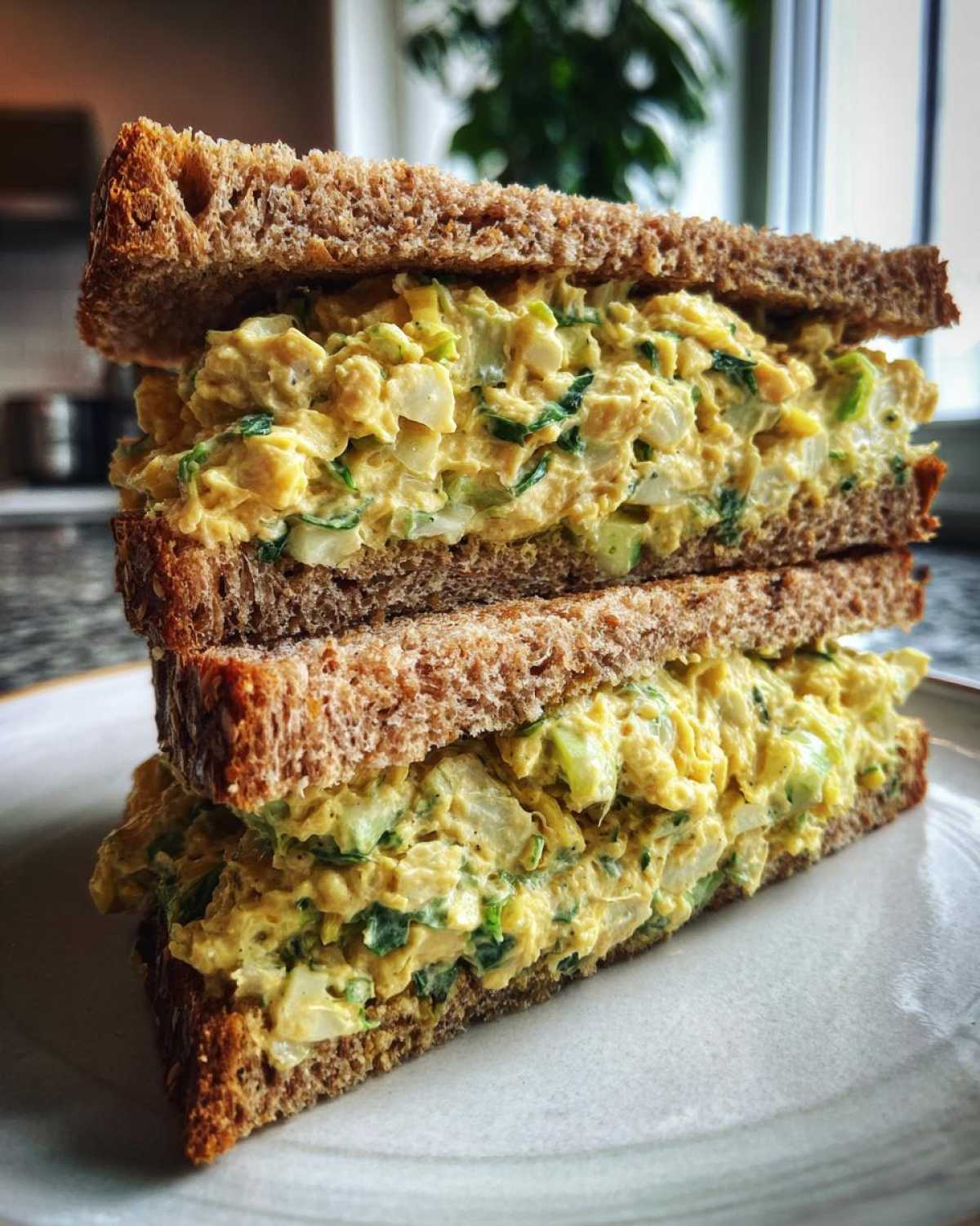 A close-up of a stacked Vegan Chickpea Salad Sandwich made with thick whole wheat bread and creamy yellow filling.
