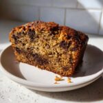 A close-up slice of moist Vegan Chocolate Banana Bread loaded with dark chocolate chips on a small white plate.