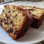 Two moist slices of Vegan Chocolate Banana Bread studded with melted chocolate chips, served on a white plate.