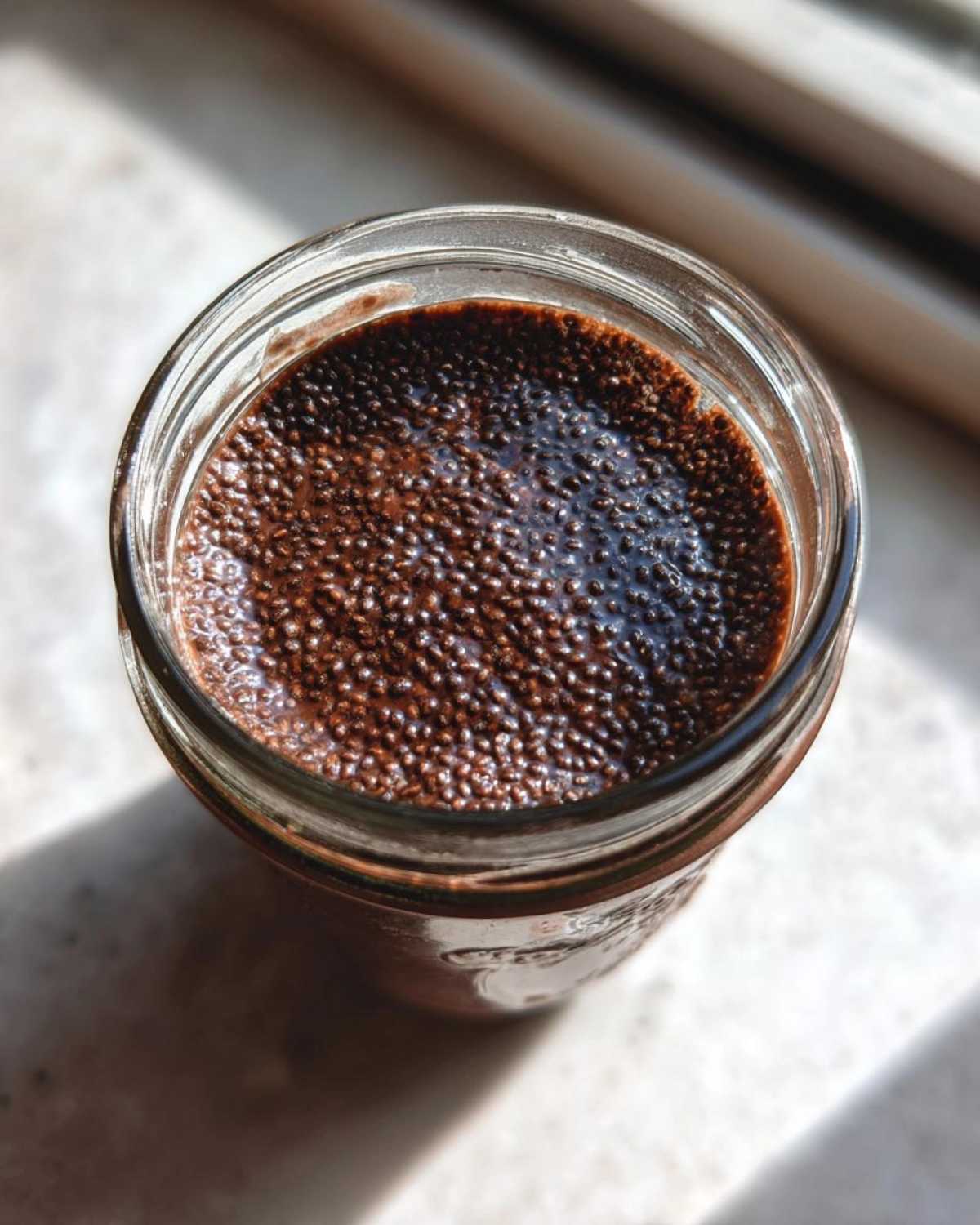 Overhead close-up of rich Vegan Chocolate Chia Pudding showing the texture of hydrated chia seeds in a glass jar.