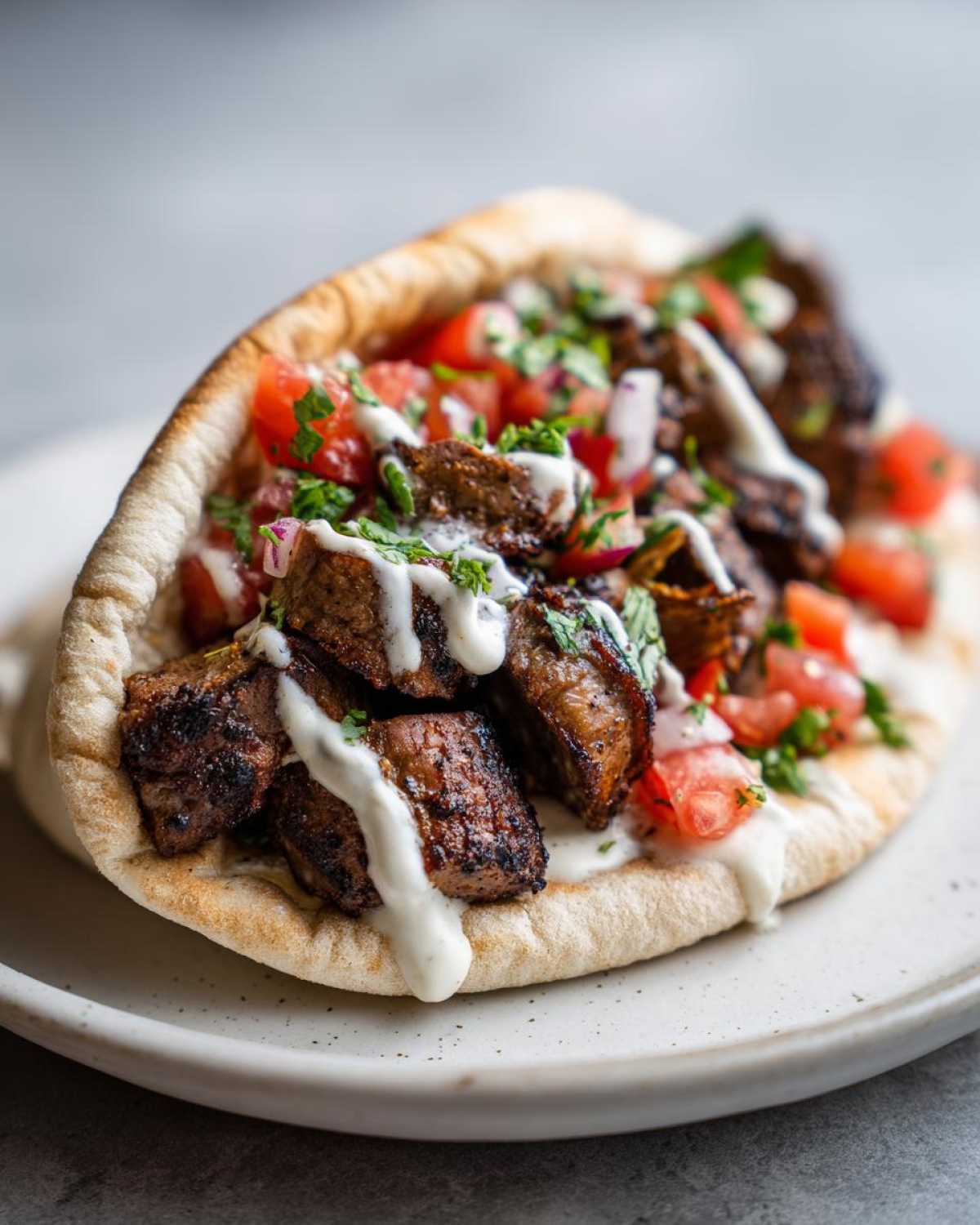 Close-up of Vegan Mushroom Shawarma filling served in a pita pocket, drizzled with white sauce and topped with tomatoes and herbs.