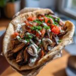 Close-up of a delicious Vegan Mushroom Shawarma stuffed into pita bread with white sauce and diced tomatoes.