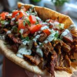 Close-up of a generously filled pita bread with savory Vegan Mushroom Shawarma, topped with fresh salsa and white sauce.