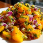 Close-up of bright orange chunks of mango mixed with diced red onion and fresh cilantro in a vibrant Spicy Mango Salsa.