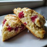 Two halves of a freshly baked White Chocolate Raspberry Scones, showing bright red raspberries and drizzled with white chocolate glaze.
