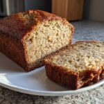 A loaf of freshly baked Banana Bread, partially sliced, showing its moist interior texture.