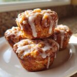A stack of three golden brown apple fritter muffins generously drizzled with a simple white glaze.