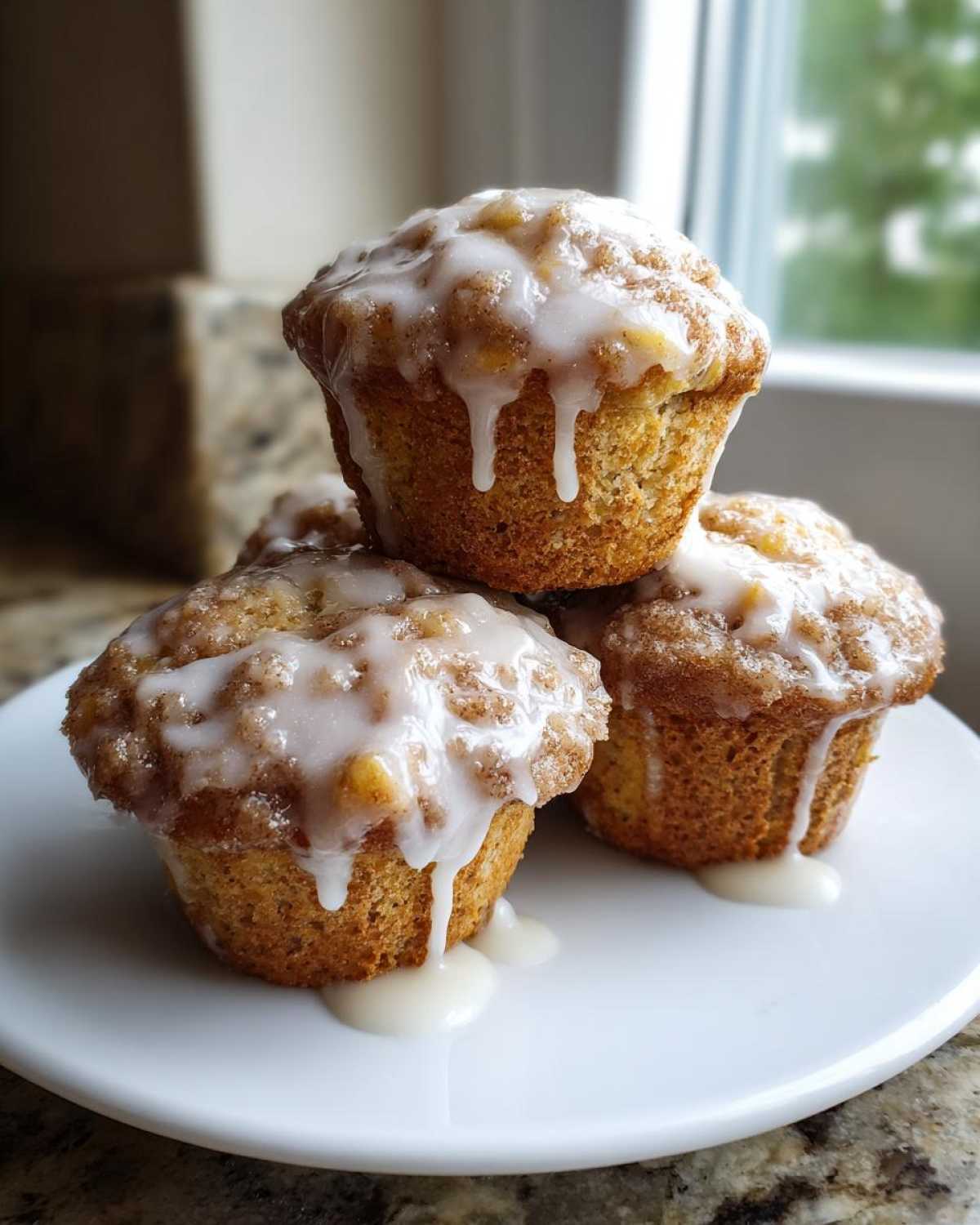 A stack of three golden Apple Fritter Muffins generously topped with a dripping simple glaze.