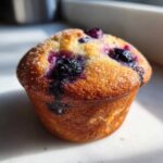 Close-up of a perfectly baked Bakery Style Blueberry Muffin with a golden crust and visible sugar crystals.