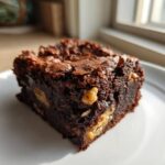 A close-up, sunlit view of a rich, fudgy Banana Bread Brownies with Walnuts square on a white plate.