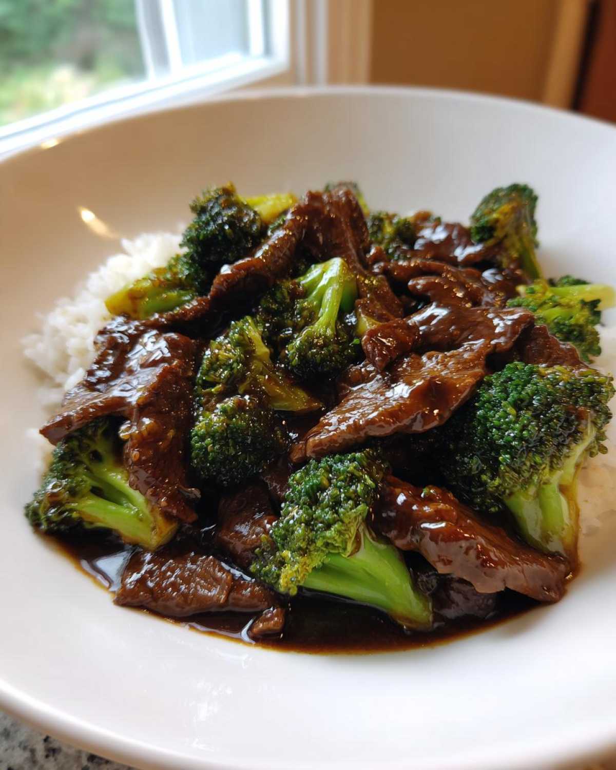 Close-up of tender slices of beef and bright green broccoli florets coated in rich sauce, served over white rice in a bowl, showcasing Beef and Broccoli Stir Fry.