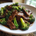 A close-up, appetizing photo of glossy Beef and Broccoli Stir Fry served in a white bowl.